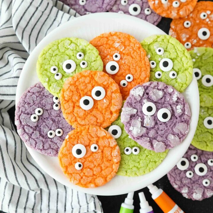 Bright colored Halloween cookies on a plate with powdered sugar cracks and candy eyeballs.