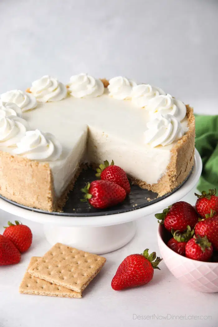 No bake cheesecake on a cake plate with a couple slices taken out and fresh strawberries on the side.