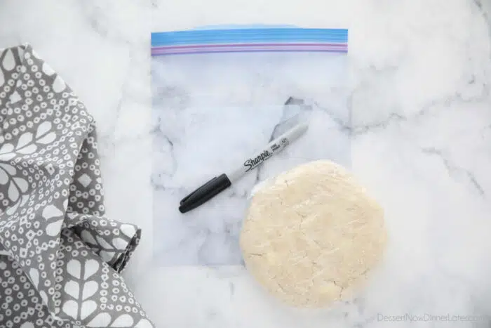 Pie crust wrapped in plastic wrap on top of a freezer bag with a sharpie for labeling.