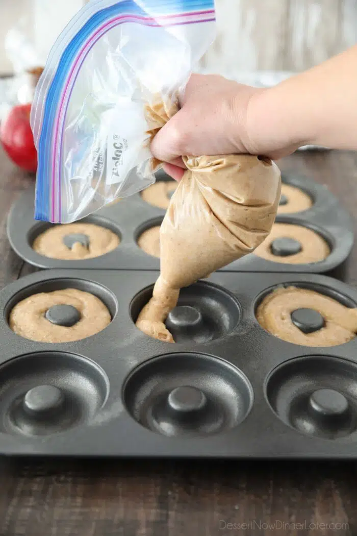 Piping apple cider cake batter into donut pans.