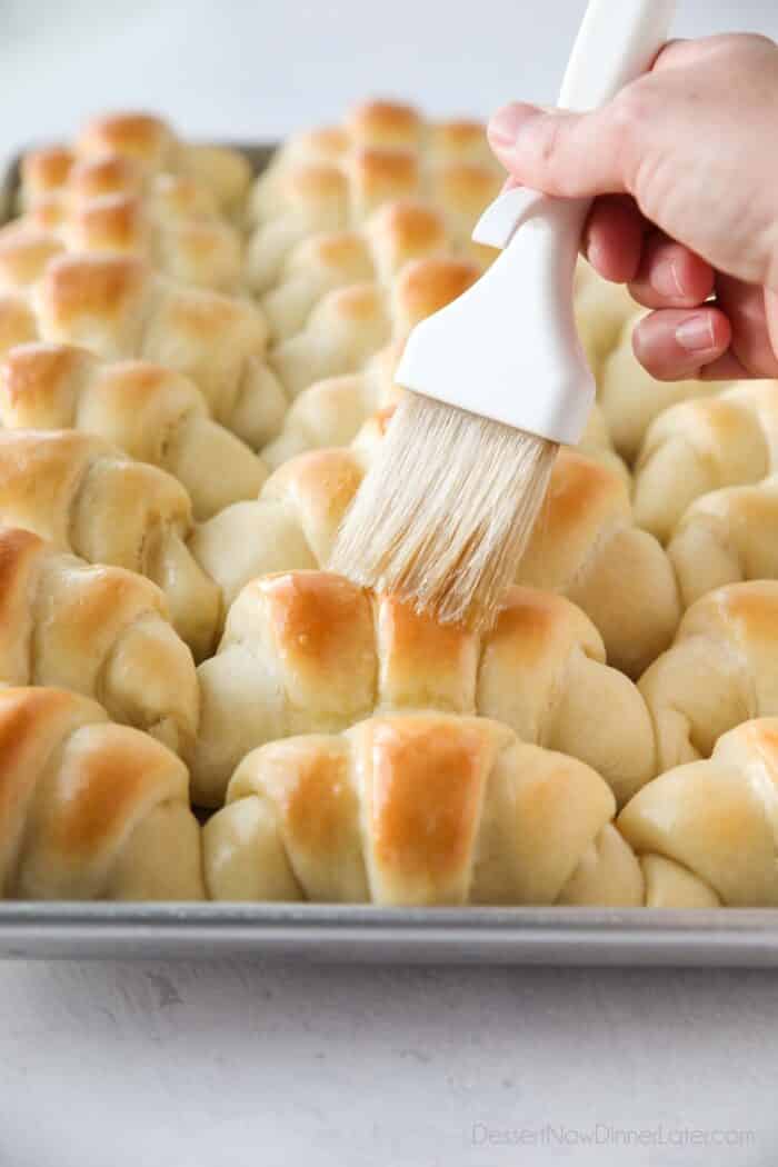 Brushing butter on top of hot crescent rolls.