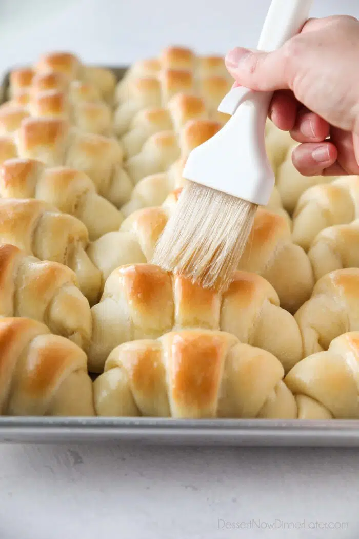 Brushing butter on top of hot crescent rolls.