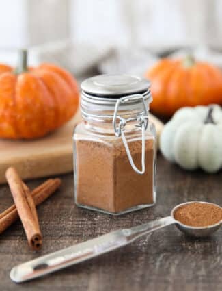 Homemade Pumpkin Pie Spice in a glass jar with mini pumpkins and cinnamon sticks on the side.