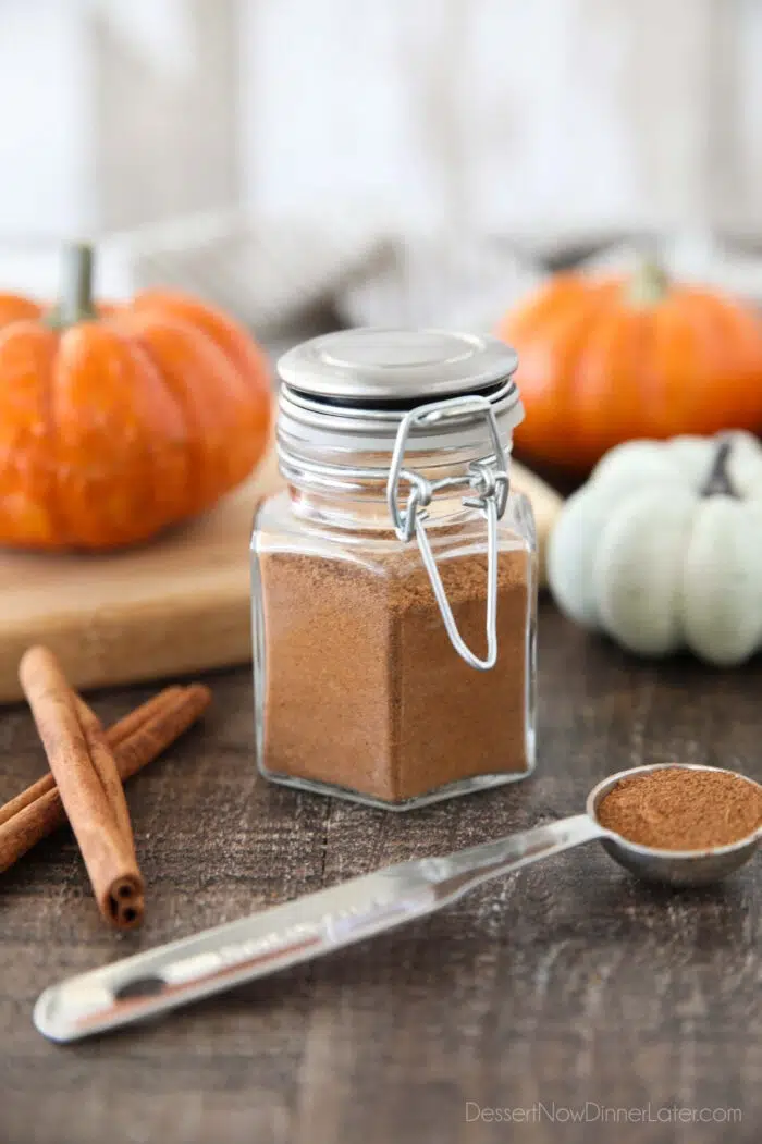 Homemade Pumpkin Pie Spice in a glass jar with mini pumpkins and cinnamon sticks on the side.