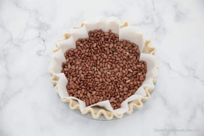 Parchment paper fitted in pie crust with dry beans on top for weights.