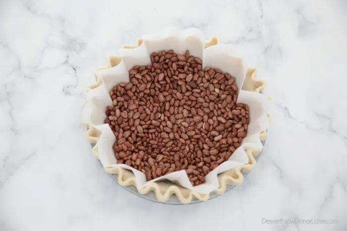 Parchment paper fitted in pie crust with dry beans on top for weights.