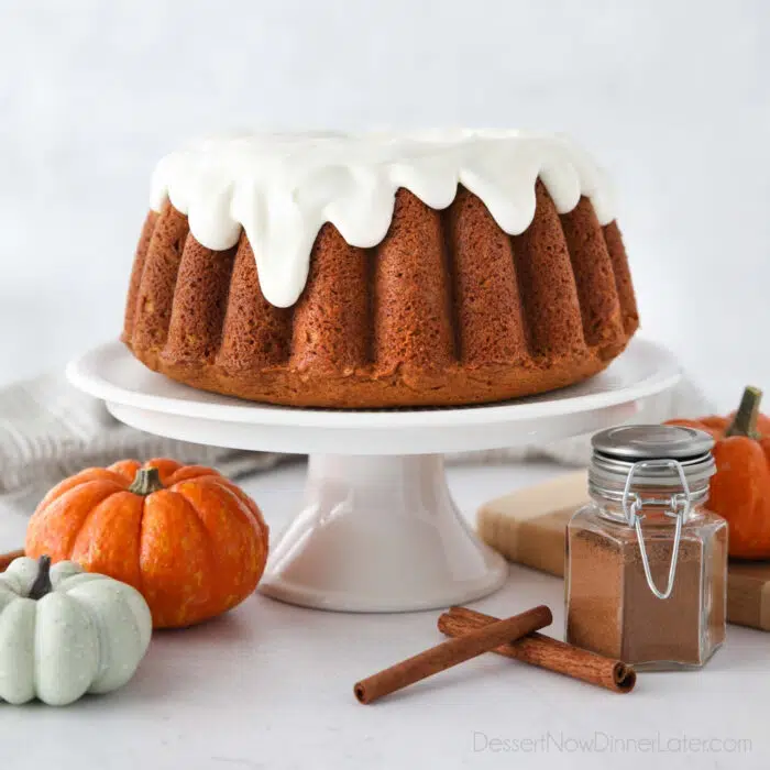 Cake stand with pumpkin bundt cake topped with cream cheese frosting.