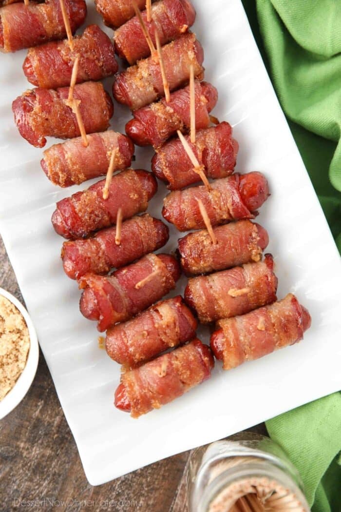 Platter of bacon wrapped cocktail weenies with toothpicks inserted.