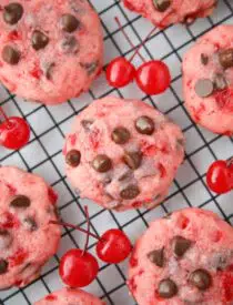 Close up top view of cherry chocolate chip cookies on a wire cooling rack with maraschino cherries on the side.