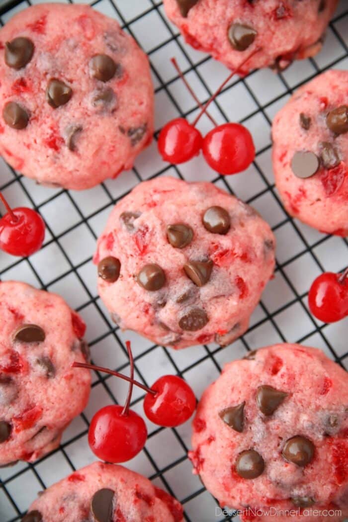 Close up top view of cherry chocolate chip cookies on a wire cooling rack with maraschino cherries on the side.