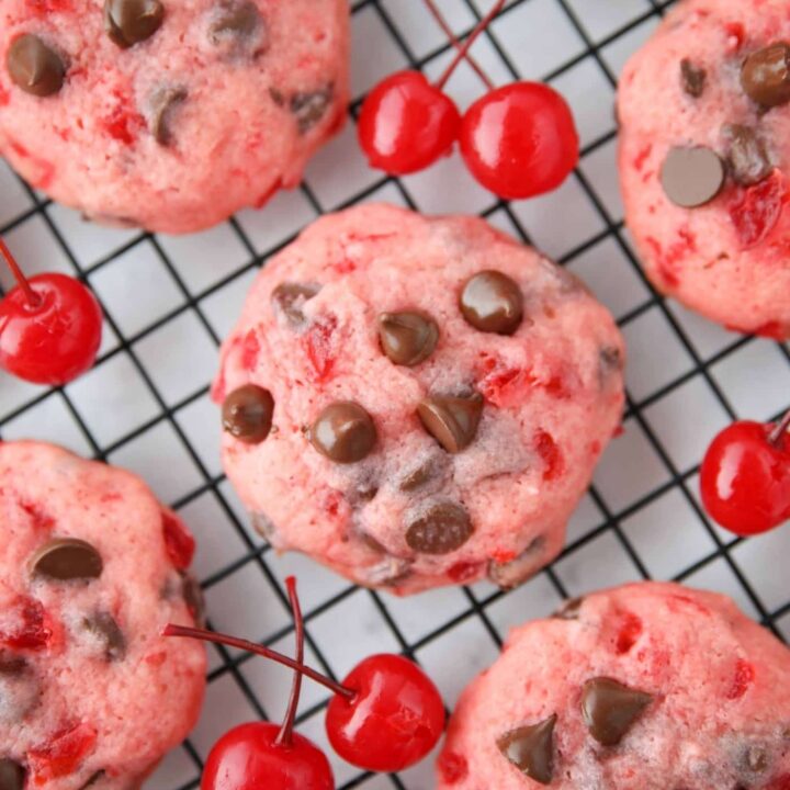 Close up top view of cherry chocolate chip cookies on a wire cooling rack with maraschino cherries on the side.