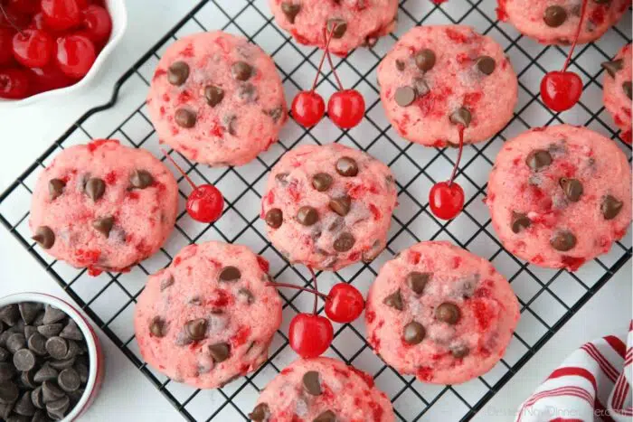 Close up top view of cherry chocolate chip cookies on a wire cooling rack with maraschino cherries on the side.