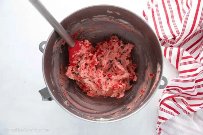 Pink cherry chocolate chip cookie dough in mixing bowl with spatula.
