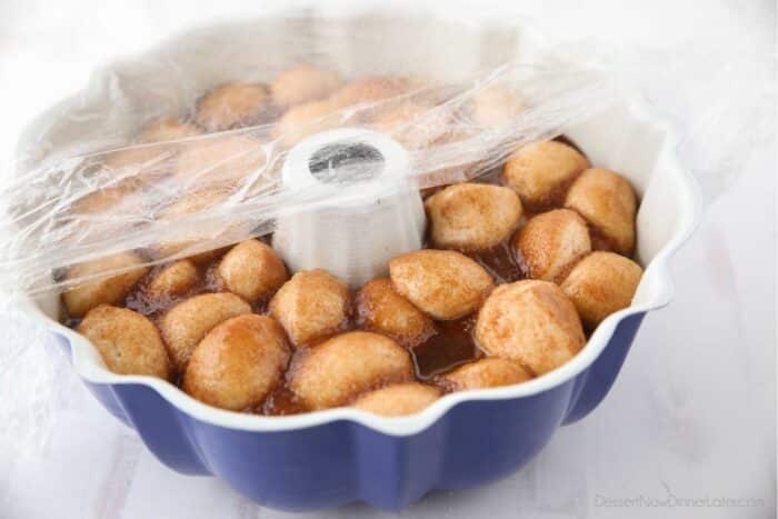 Monkey bread rising in pan with greased plastic wrap on top.
