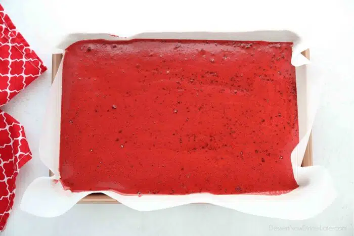 Red velvet cake batter poured into jelly roll pan lined with parchment paper.
