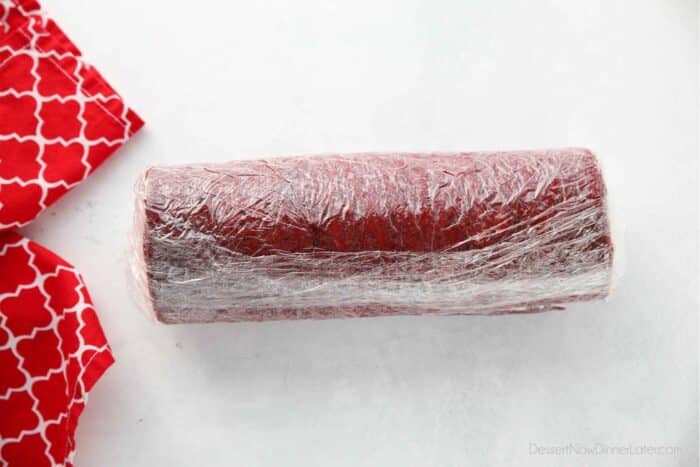 Red velvet cake roll wrapped in plastic wrap to be chilled in fridge or freezer.