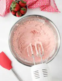 Strawberry cream cheese frosting in bowl with electric mixer and beaters.