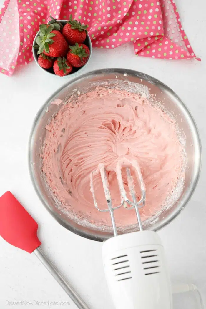 Strawberry cream cheese frosting in bowl with electric mixer and beaters.