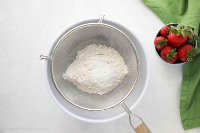 Sifting dry ingredients into a bowl with a fine mesh sieve.