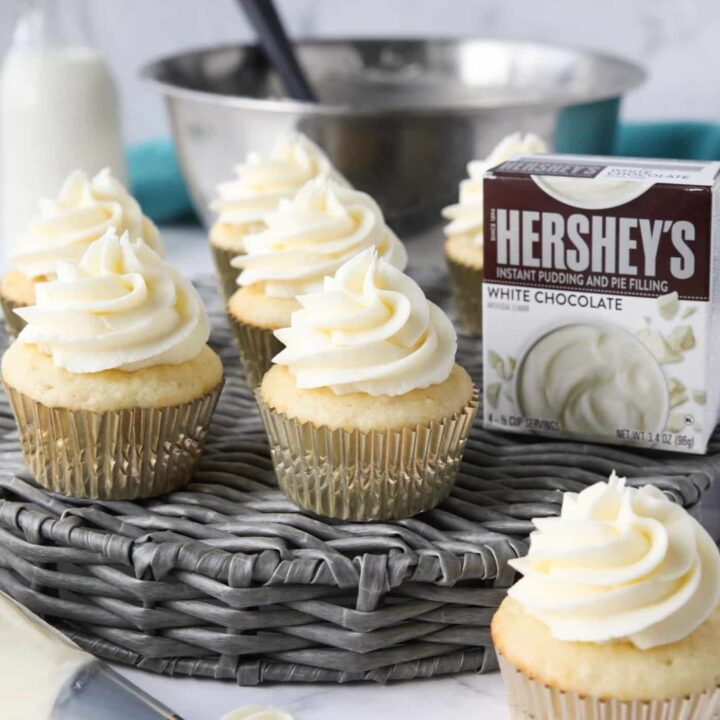 Cupcakes topped with white chocolate pudding buttercream frosting made with instant pudding mix.