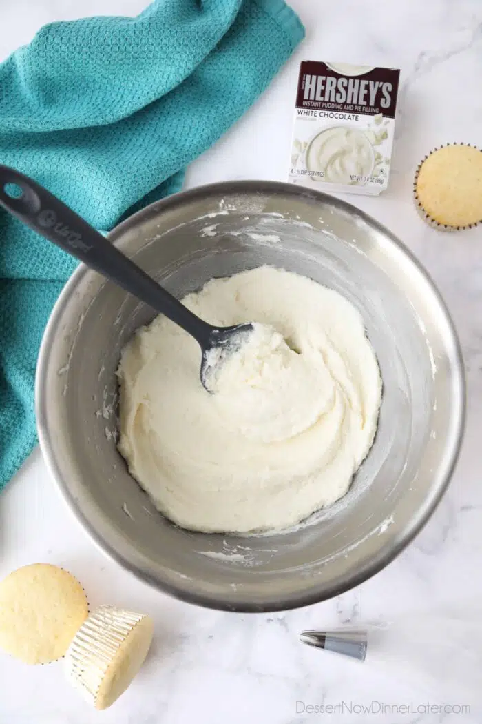 Bowl of pudding frosting with a spatula inserted and a box of Hershey's white chocolate instant pudding mix.