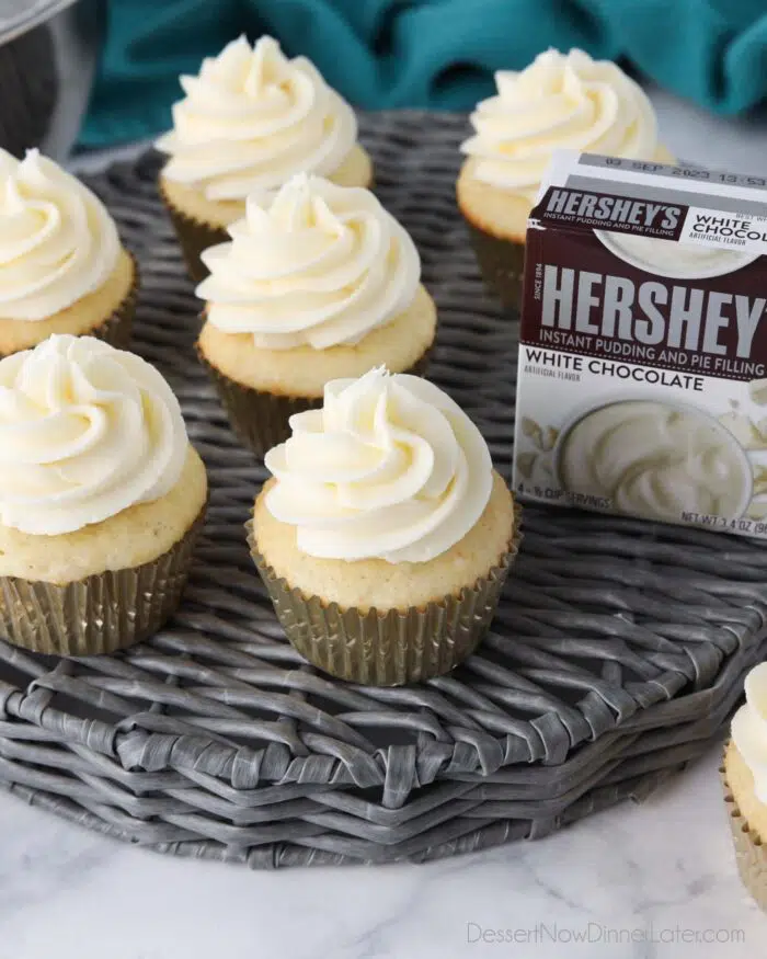 Close up top view of white chocolate pudding frosting on top of white cupcakes and a box of Hershey's instant pudding.