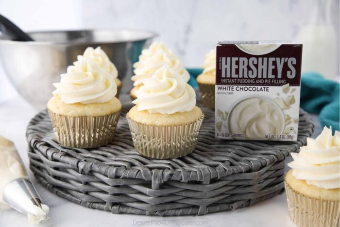 Front view of cupcakes topped with pudding buttercream frosting and a box of white chocolate pudding mix.