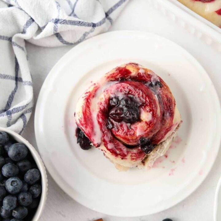 Top view of single blueberry cinnamon roll on a plate.