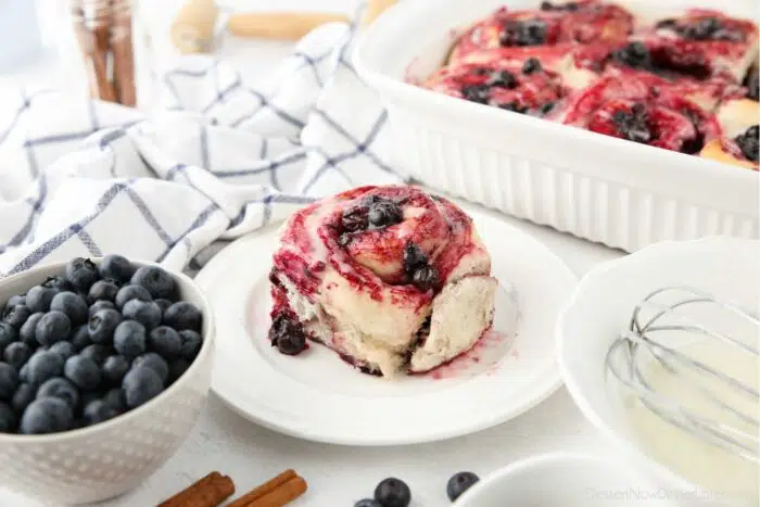 Side view of a cinnamon roll topped with whole blueberry sauce.