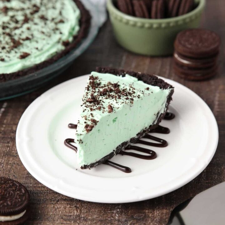 Slice of mint grasshopper pie with an Oreo crust on top of a plate drizzled with chocolate sauce.