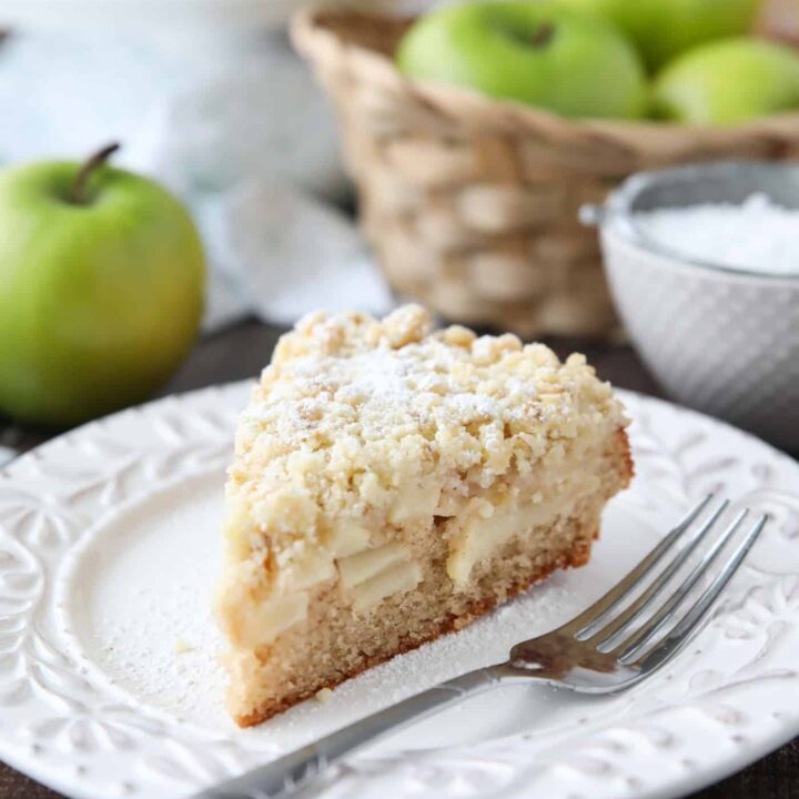 Slice of apple cake on a plate with crunchy streusel on top.