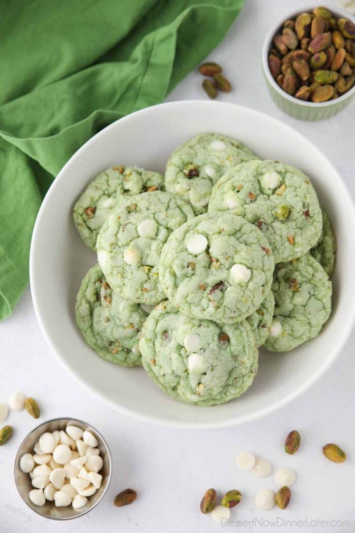 Plate full of green pistachio cookies with white chocolate chips and pistachio nuts.