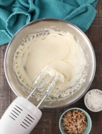 Mixing bowl and beaters filled with coconut cream cheese frosting.