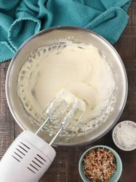 Mixing bowl and beaters filled with coconut cream cheese frosting.