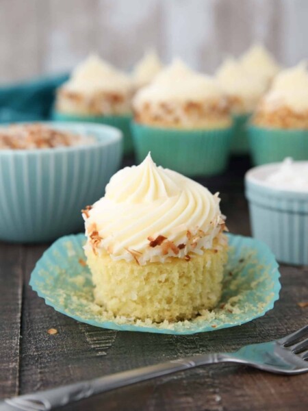 Paper wrapper pulled down exposing the crumb of a coconut cupcake.