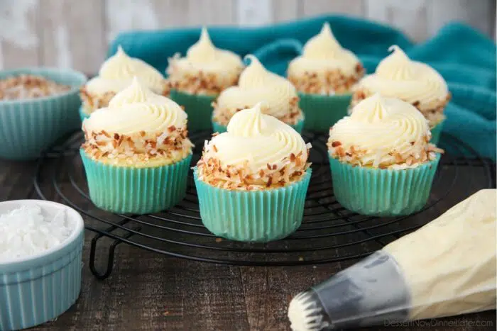 Side view of coconut cupcakes topped with frosting and toasted coconut on a wire cooling rack.