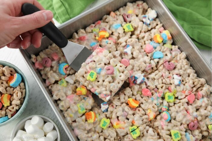 Scooping a lucky charms marshmallow treat out of the pan.