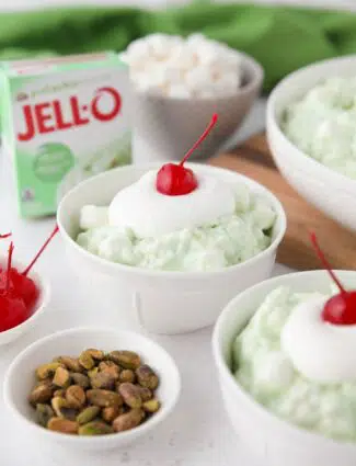 Close up of pistachio fluff in a bowl with whipped cream and a cherry on top.