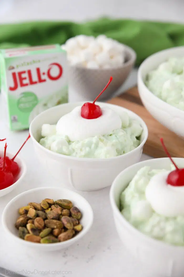 Close up of pistachio fluff in a bowl with whipped cream and a cherry on top.