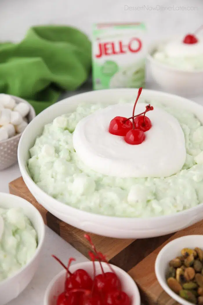 Big bowl full of pistachio fluff topped with whipped cream and maraschino cherries.