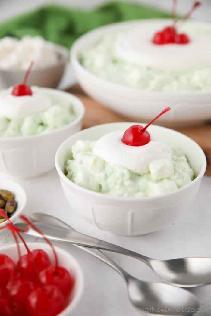 Bowls of watergate salad with whipped cream and cherries on top.