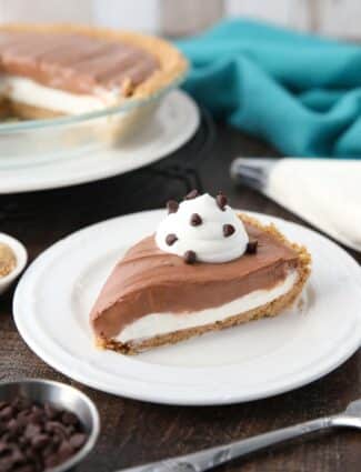 Slice of pie on a plate with a graham cracker crust, and layers of vanilla and chocolate no-bake cheesecake with whipped cream and mini chocolate chips on top.