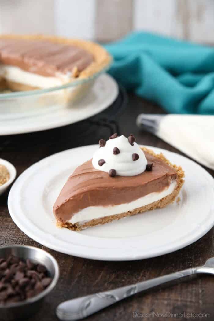 Slice of pie on a plate with a graham cracker crust, and layers of vanilla and chocolate no-bake cheesecake with whipped cream and mini chocolate chips on top.
