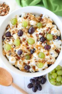 Top view of a creamy fruit salad with red and green grapes, pecans, and brown sugar.