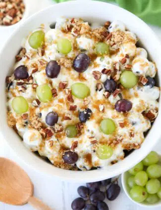 Top view of a creamy fruit salad with red and green grapes, pecans, and brown sugar.