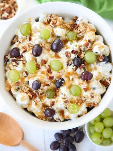 Top view of a creamy fruit salad with red and green grapes, pecans, and brown sugar.