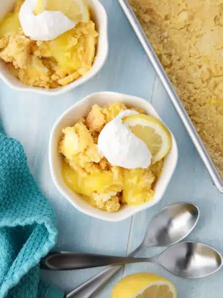 Lemon Dump Cake in a small bowl topped with whipped topping and a lemon slice.