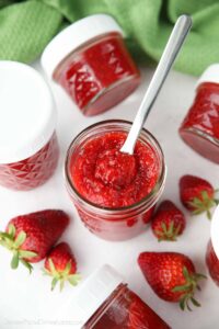 Top view of an open jar of low-sugar strawberry jam with a spoon inside.