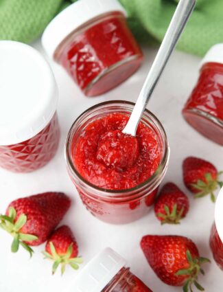 Top view of an open jar of low-sugar strawberry jam with a spoon inside.