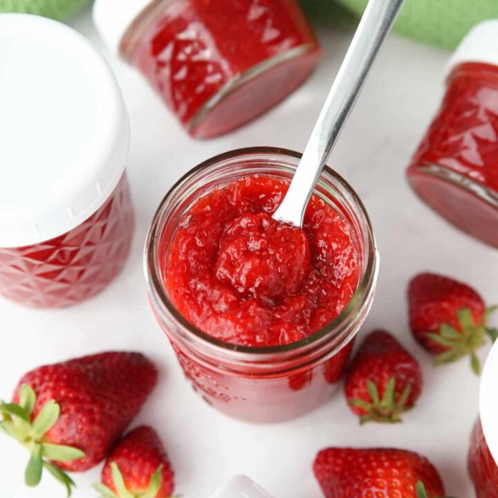 Top view of an open jar of low-sugar strawberry jam with a spoon inside.
